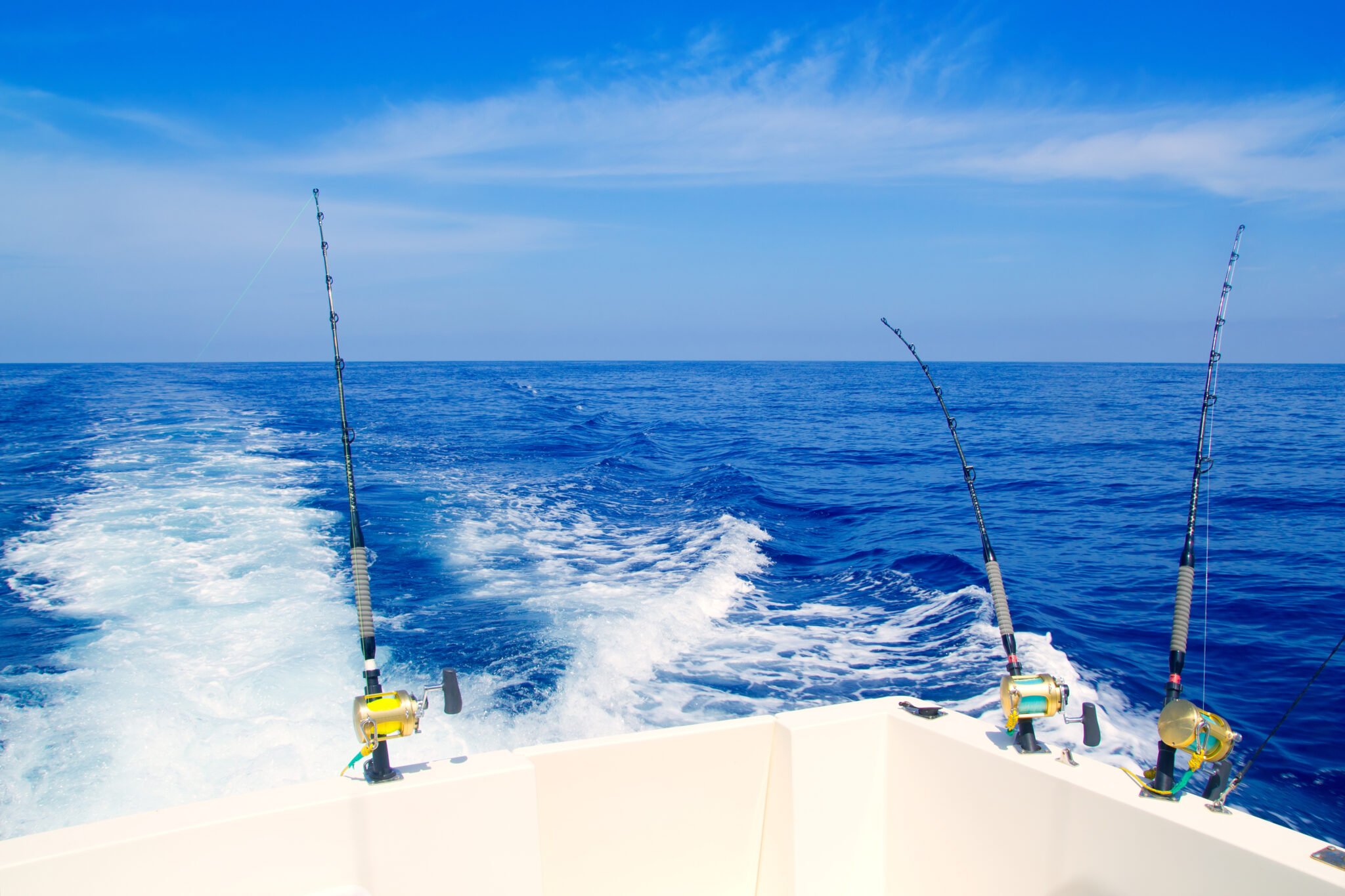 "A boat fishing by trolling in the deep blue sea, equipped with rods and reels. Honolulu Fishing Charters. 